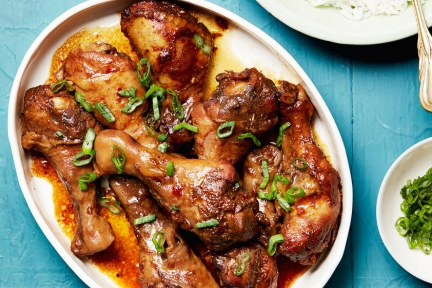Slow cooker Asian style drumsticks on a white dish topped with green onions