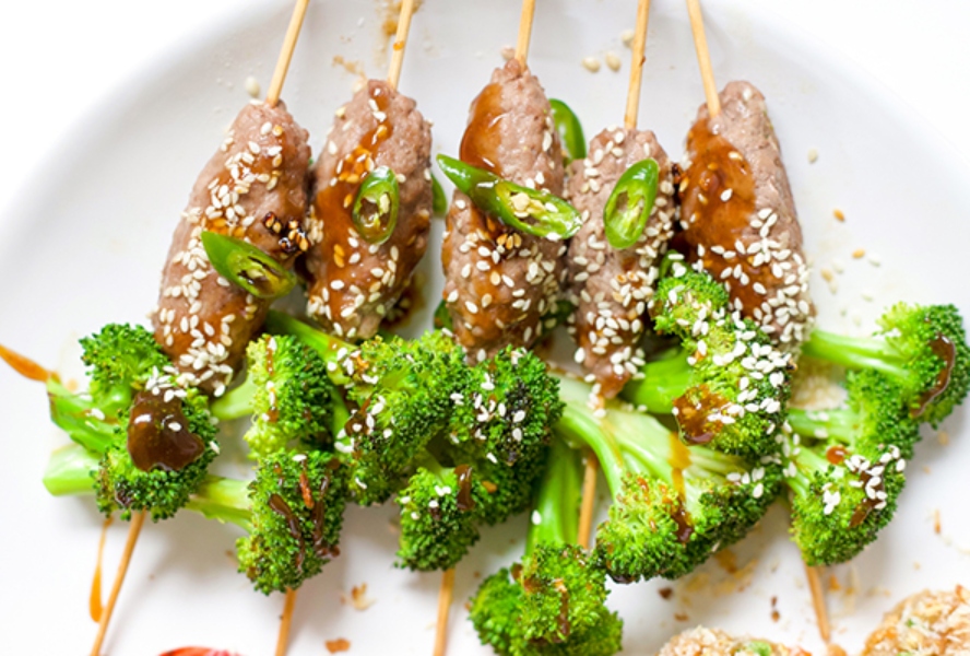 Slices of beef and broccoli florets on wooden skewers with teriyaki sauce