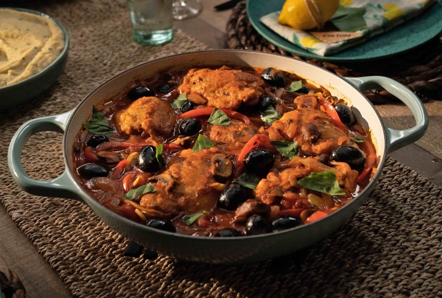 A pan with chicken, mushrooms, olives and capers in tomato sauce