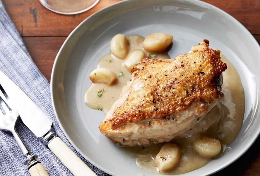 A chicken breast cooked to a golden finish with whole cloves of garlic and a creamy sauce