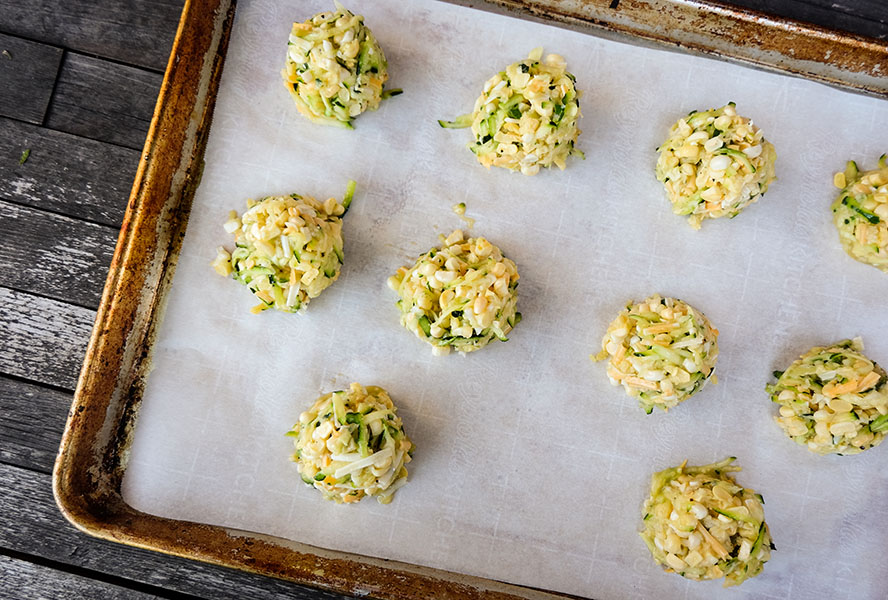 zucchini fritters scooped into balls and lined on a parchment-lined cookie sheet