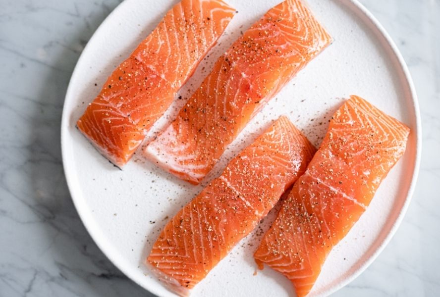 Four raw salmon filets on white plate