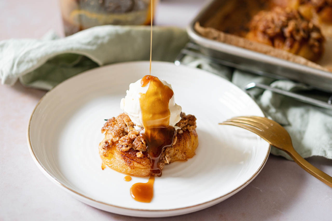 a hasselback apple topped with ice cream and toffee drizzle on a white plate