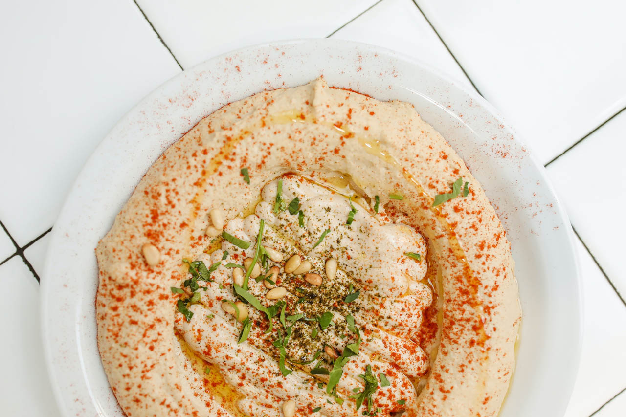 a bowl of hummus on a white tile background