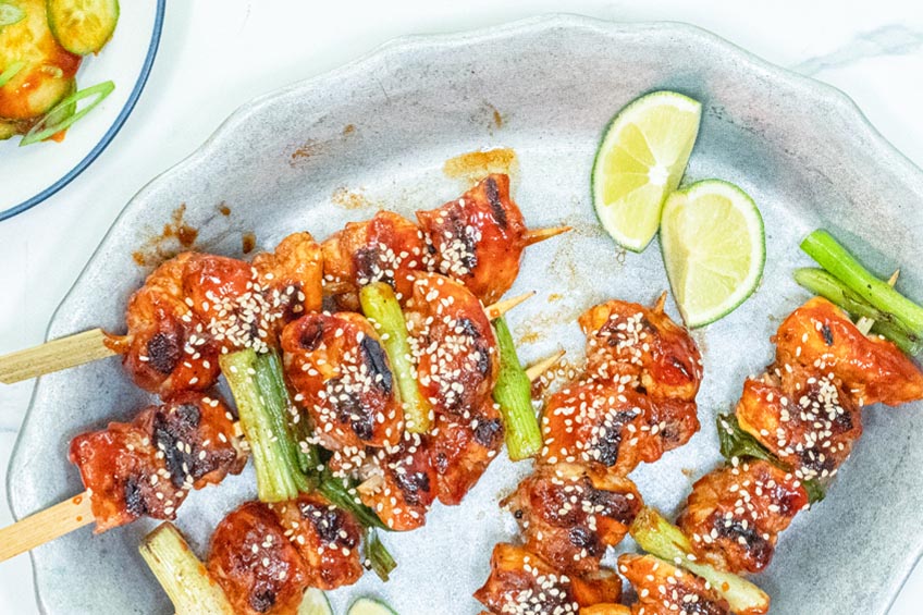 Grilled Korean Chicken Skewers topped with sesame seeds and lime on a grey plate