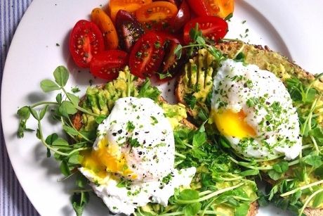 Avocado toast with eggs and tomatoes on white plate