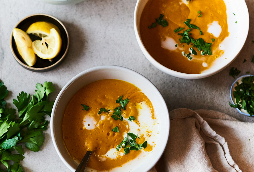 Orange pumpkin soup served in white bowls topped with fresh herbs