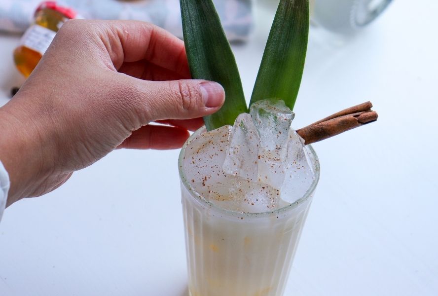 person placing leaves in non-alcoholic winter colada cocktail