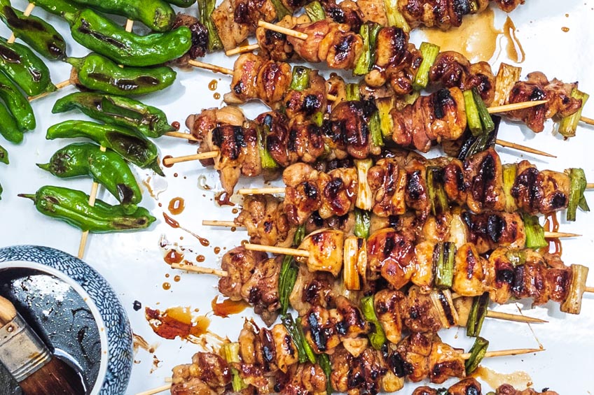 Yakitori chicken skewers alongside shishito pepper chicken skewers and a bowl of sweet, sticky glaze