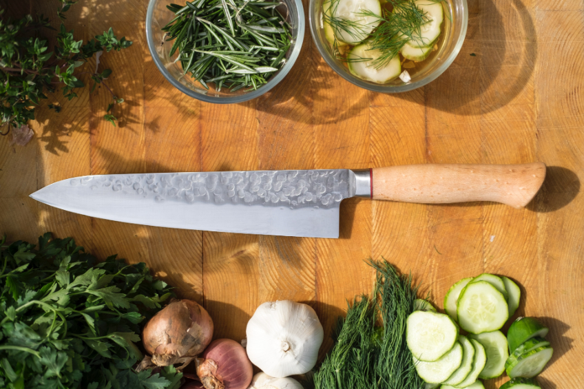A chef knife on a cutting board with various fresh produce chopped nearby
