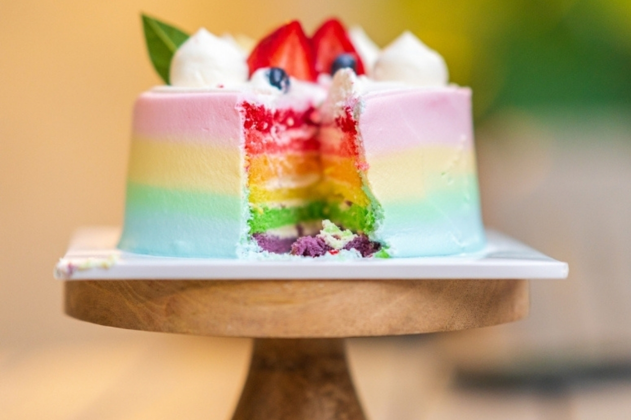 Multi-coloured cake on a cake round with a piece missing from it displayed from the side.