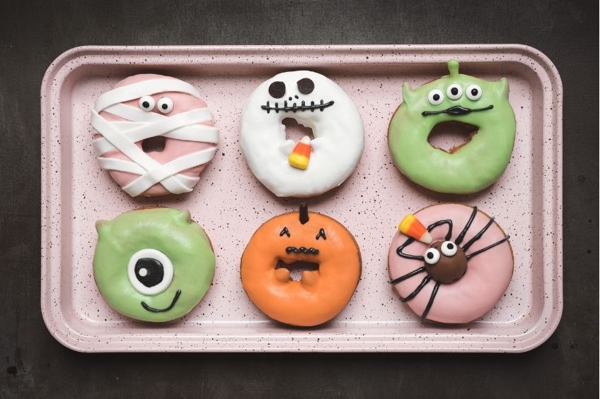 Six Halloween-themed decorated donuts on a pan sheet