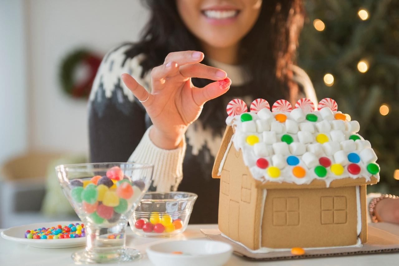 Woman decorating gingerbread house.