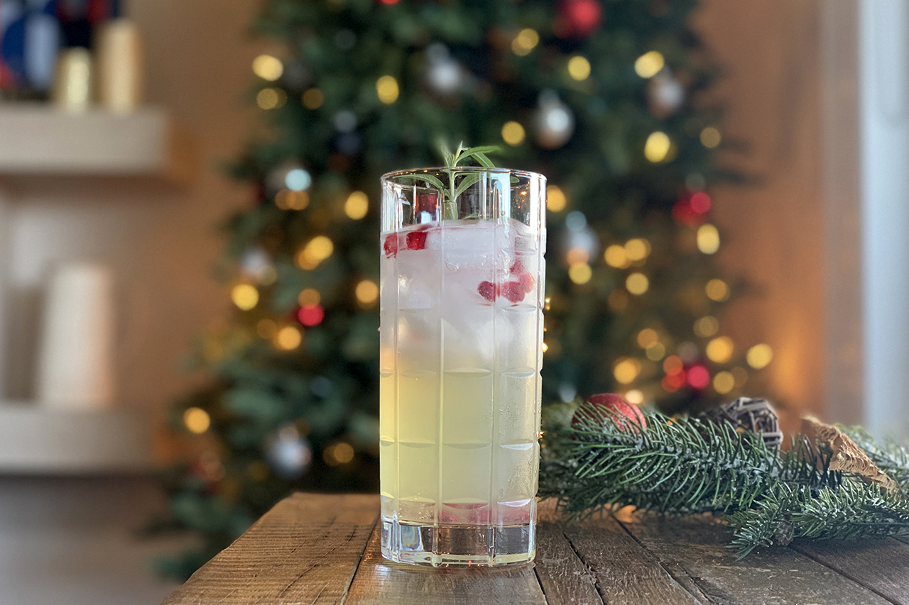 Non-alcoholic ginger-rosemary Christmas cocktail against a Christmas tree backdrop