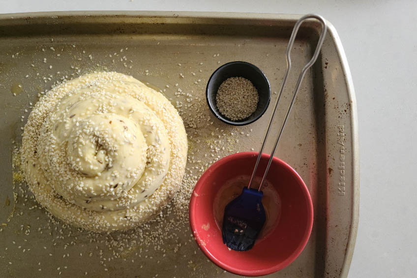 dough for sephardic challah sprinkled with sesame seeds on a baking sheet