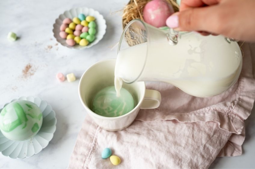 Easter egg hot chocolate bomb in cup with milk being poured on top