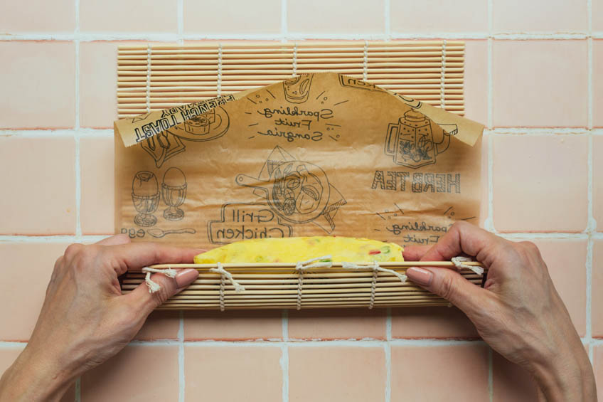 a hotdog omelette being rolled up in parchment paper and a bamboo mat