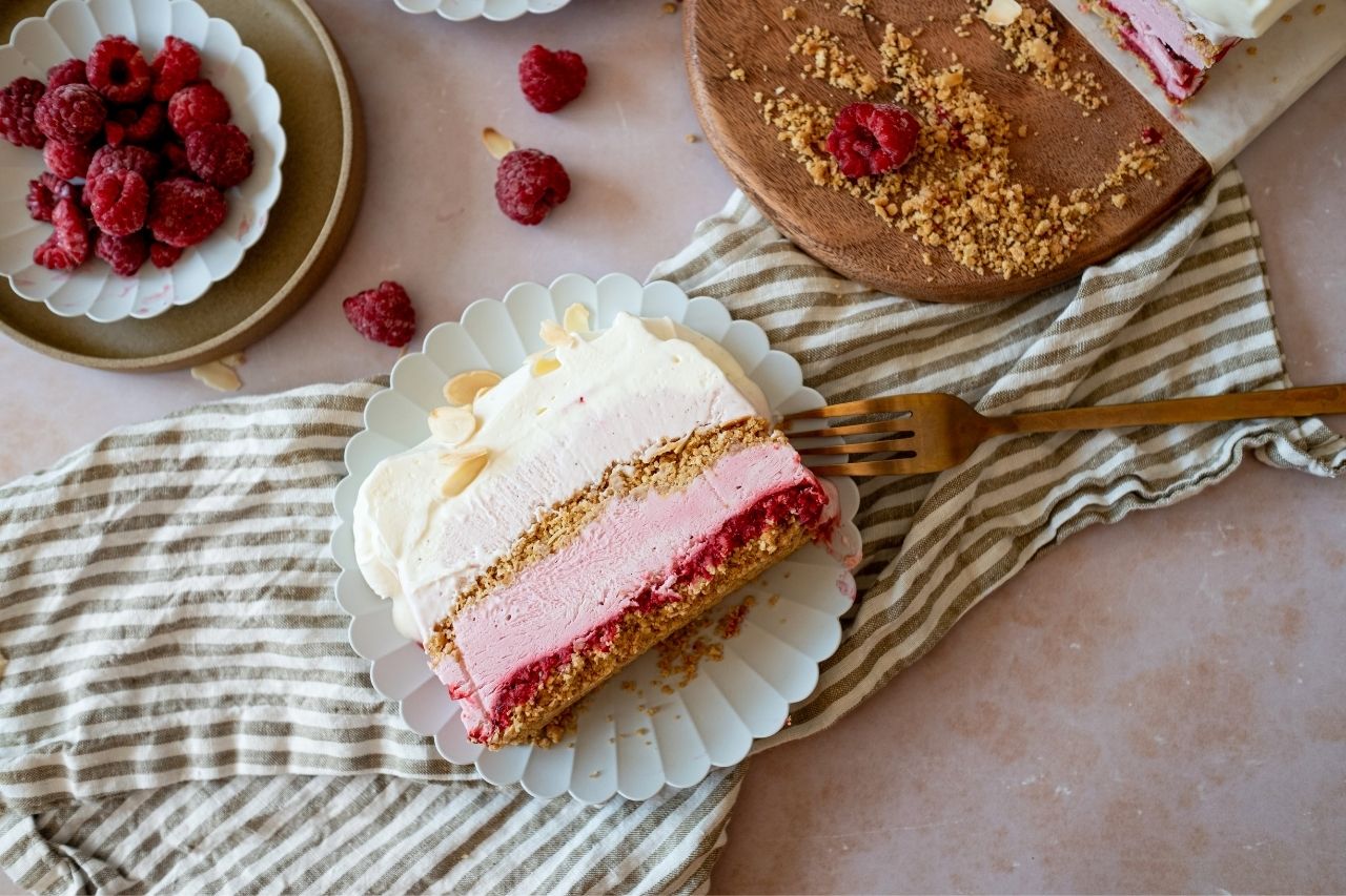 Ice cream cake on plate next to bowl of raspberries