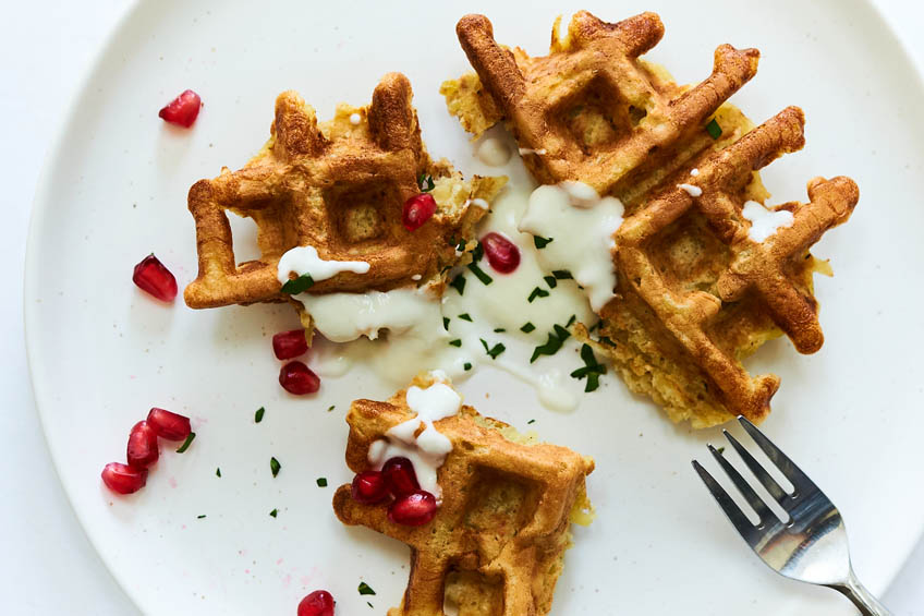 A closeup of a latke waffle topped with sour cream and pomegranate seeds