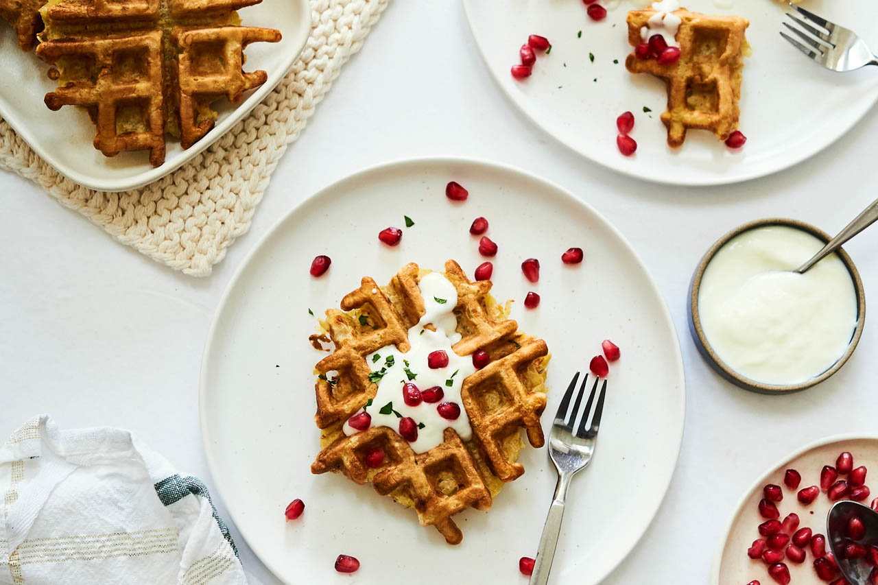 Latke waffle on a plate topped with sour cream and pomegranate seeds