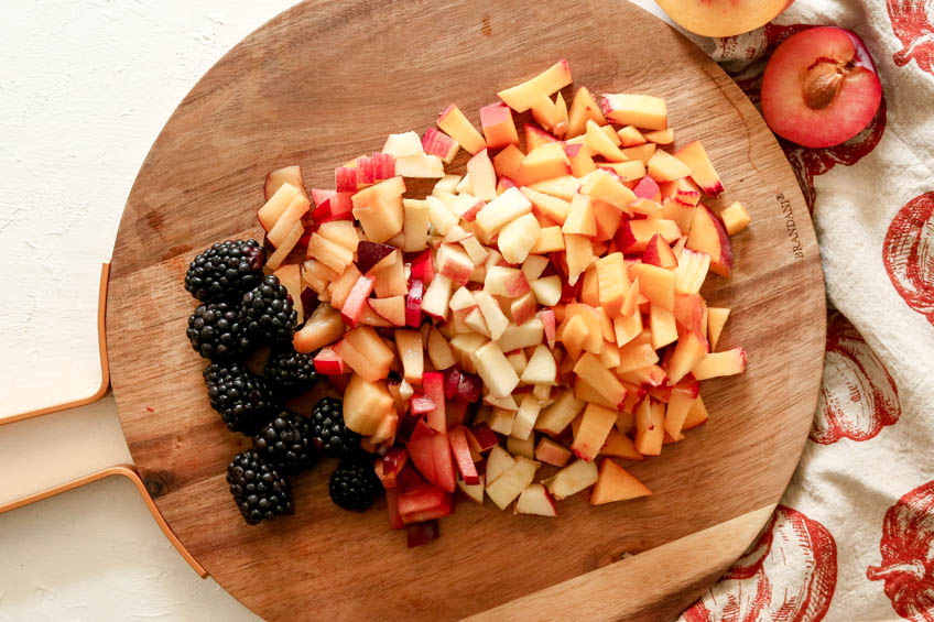 fruit salad ingredients chopped on a round wooden cutting board