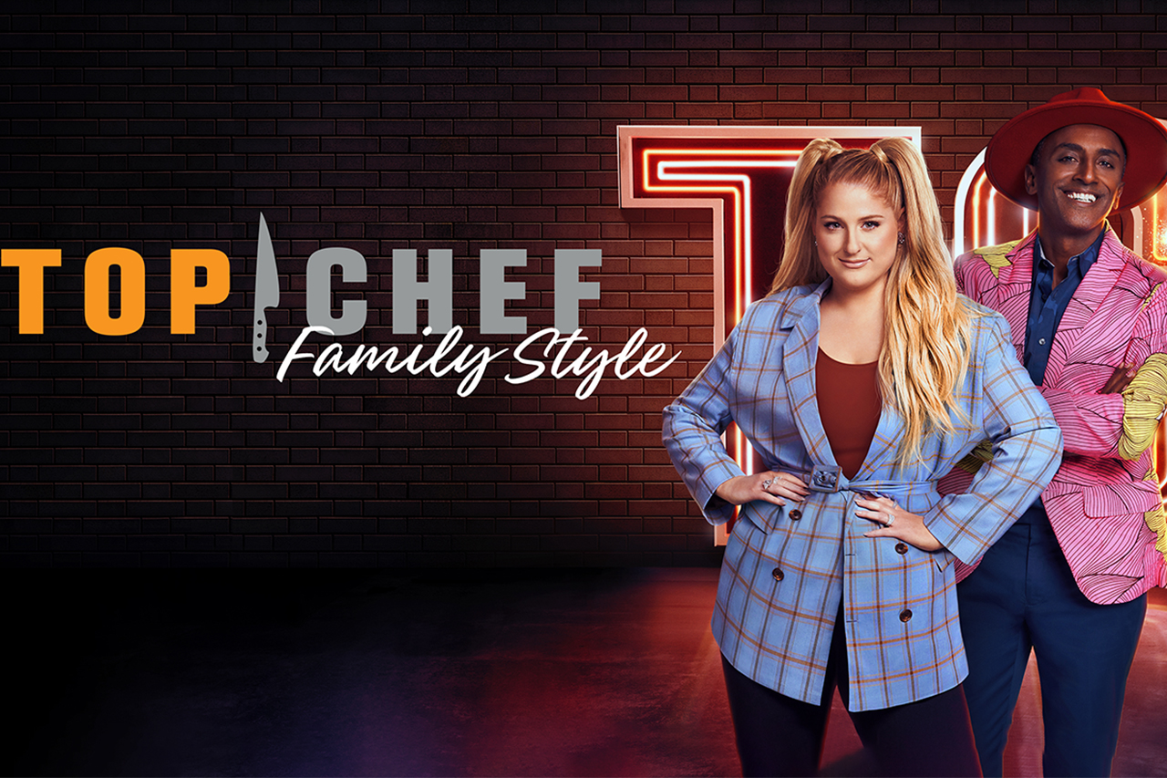 American singer Meghan Trainor and Acclaimed Chef Marcus Samuelsson smile for the camera in front of a banner that reads Top Chef Family Style