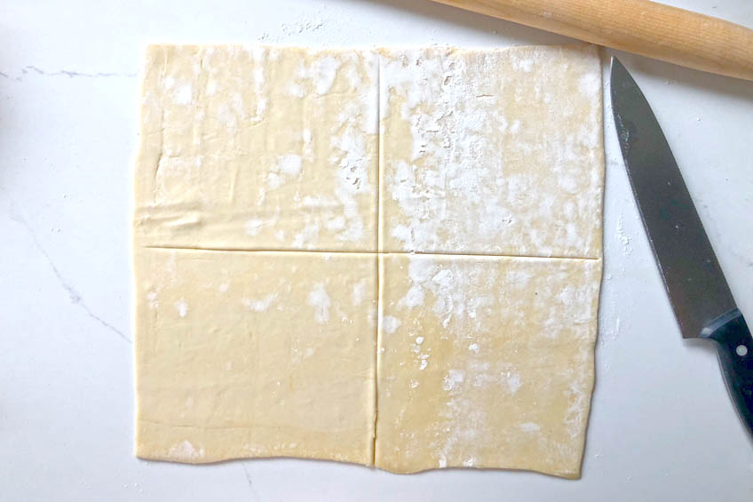 a puff pastry sheet on a white countertop cut into quarters