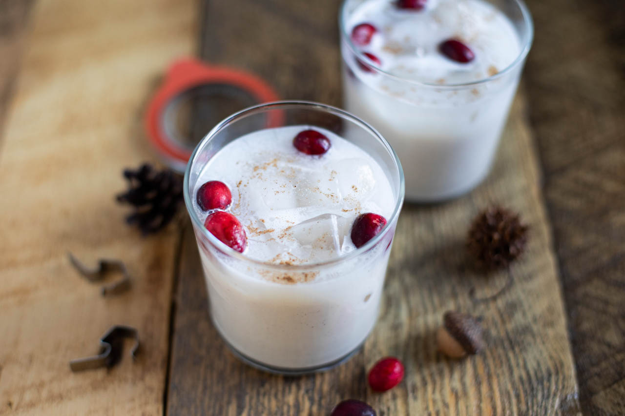 a glass of vegan eggnog with ice and cranberries