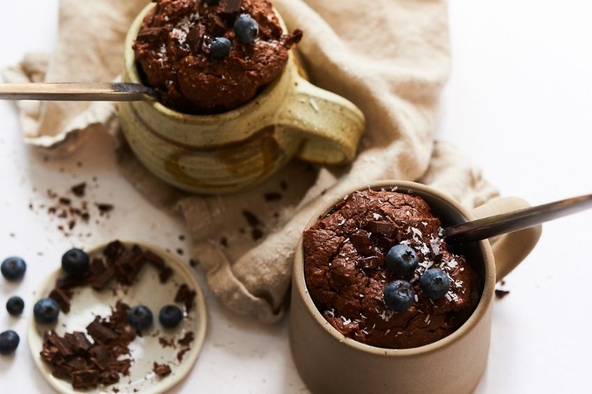 two vegan mug cakes with chocolate and blueberries on top