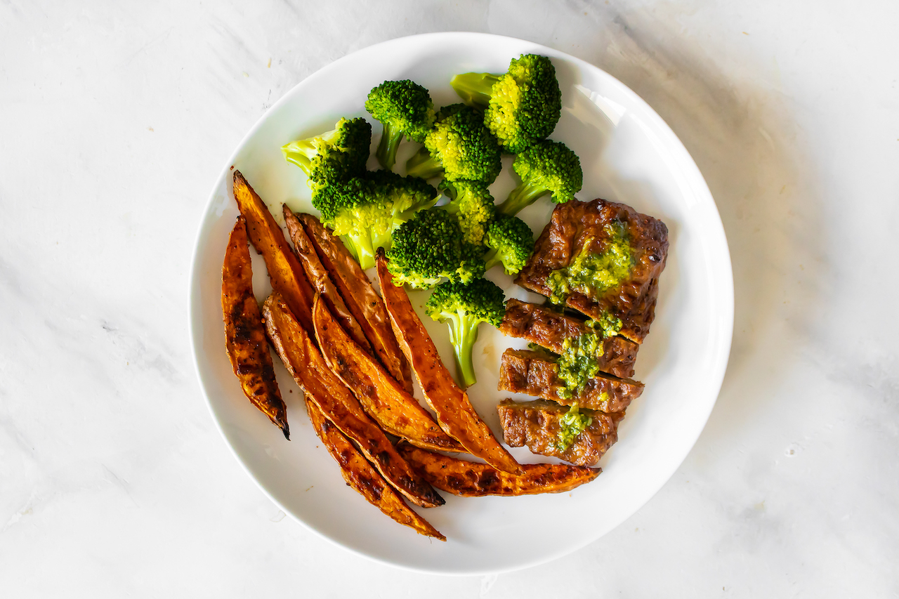 Sliced vegan steak with sweet potato and broccoli on a white plate