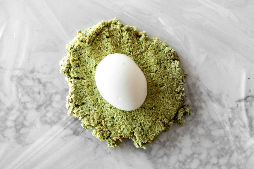 A peeled boiled egg on a bed of falafel mixture.