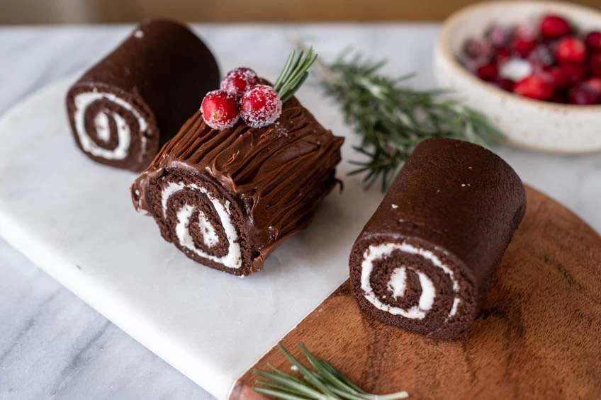 A buche de noel cake cut into three small sections, the one in the middle is iced and decorated