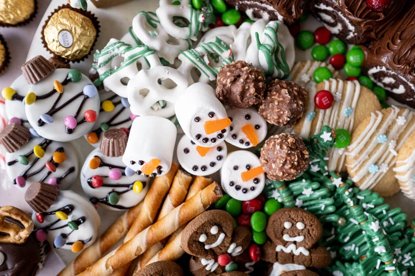 A plate of holiday sweets like cookies, marshmallow snowmen, covered pretzels and more