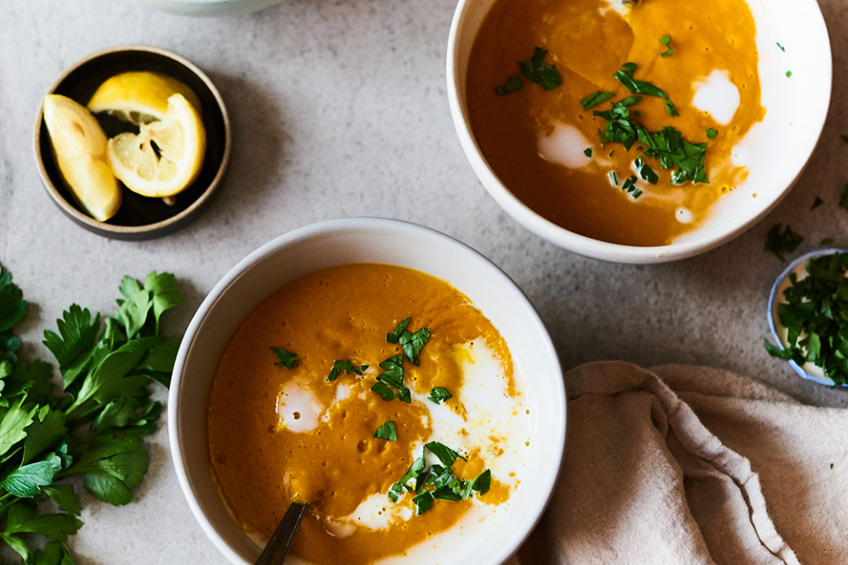Two bowls of velvety pumpkin soup topped with a drizzle of coconut milk and fresh herbs