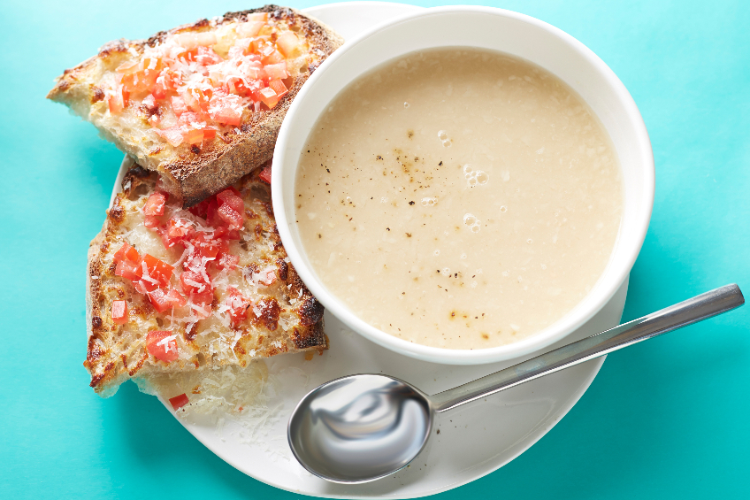 A bowl of creamy white bean soup with cheese and tomato topped toast on the side