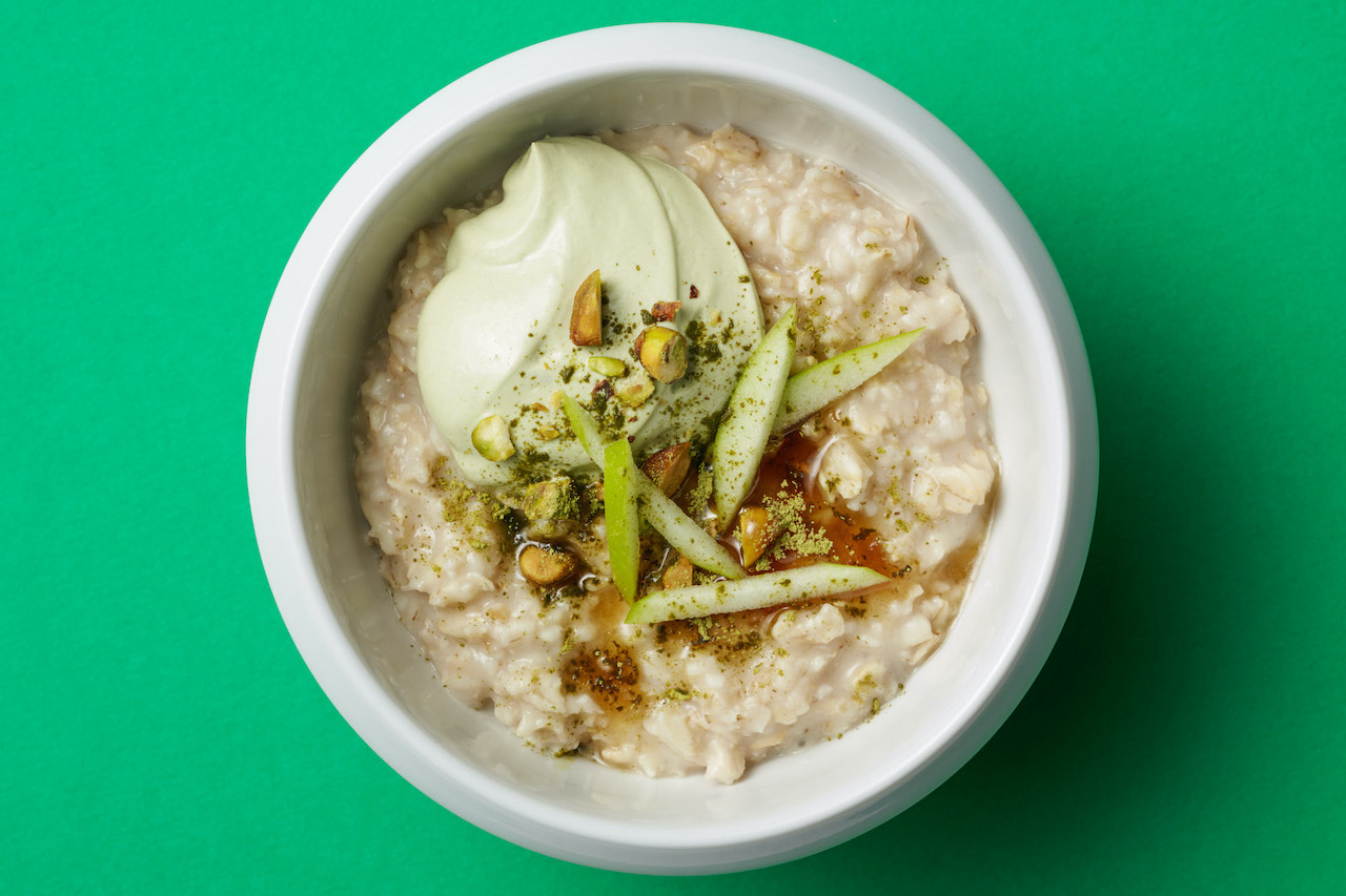 A bowl of oatmeal topped with a dollop of yogurt, pistachios and green apple