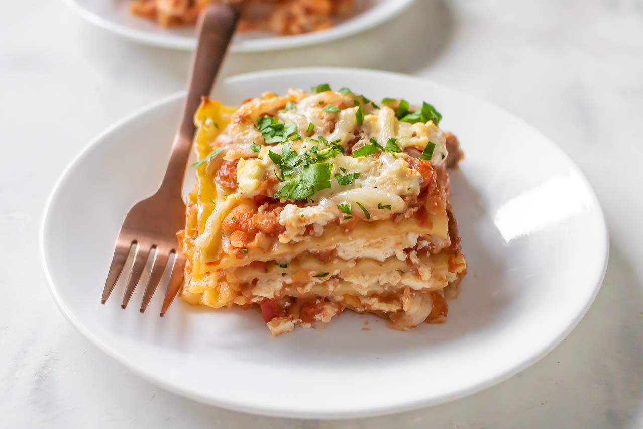A slice of vegan lasagna on a white plate with tomato-base.