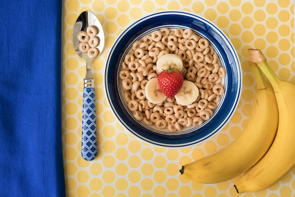 A bowl of cheerios with strawberries and bananas.