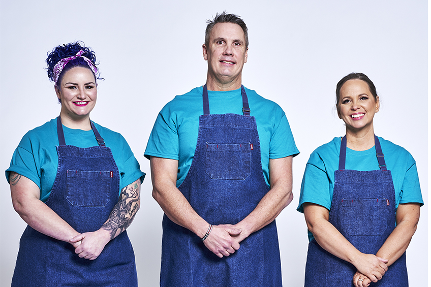 3 contestants in blue aprons looking at the camera