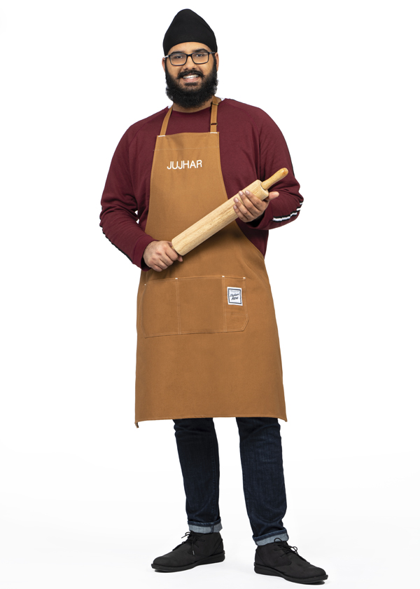 Jujhar Mann poses wearing a brown apron and holding a wooden rolling pin