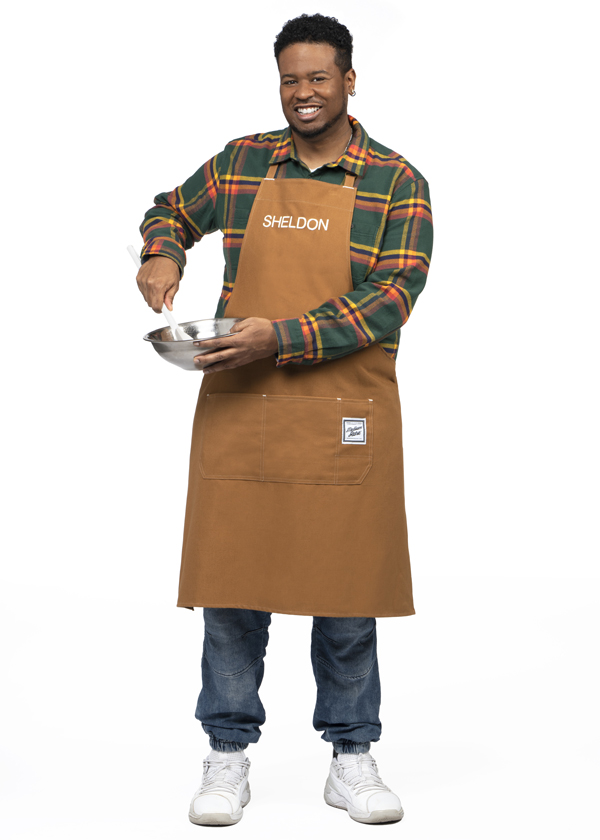 Sheldon Taylor-Timothy wearing a brown apron and holding a metal bowl and whisk