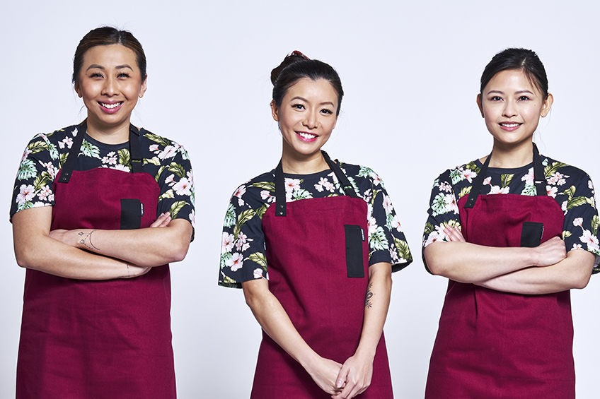 3 contestants looking at the camera and smiling wearing burgundy aprons