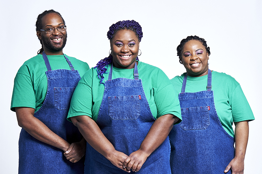3 contestants looking at the camera and smiling wearing blue aprons