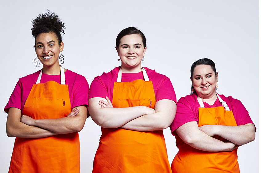 3 team members in orange aprons looing and smiling at the camera