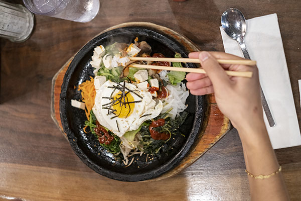 Person eating Korean bibimbap with chopsticks at a Korean restaurant. Overhead shot of hand eating.
