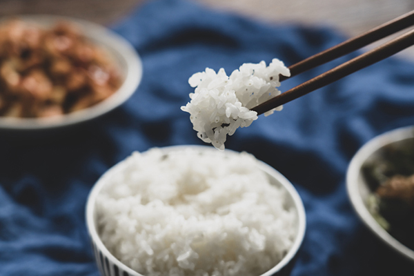 A set of chopsticks picking up white rice from a small bowl