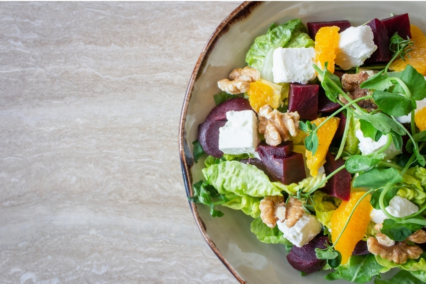 Salad made of greens, goat cheese, walnut, beets and Clementines in a bowl