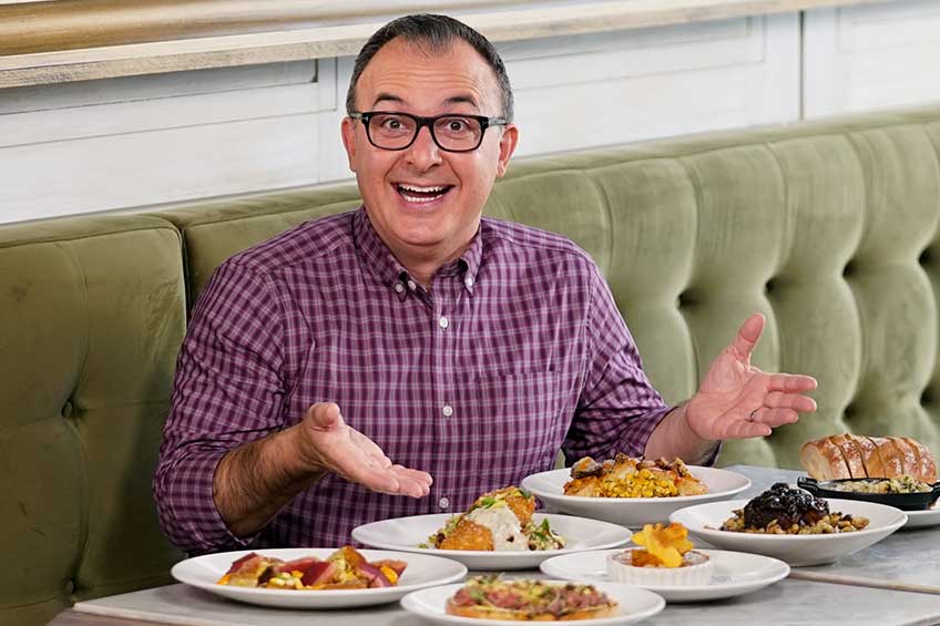 John Catucci smiling in front of a plate of dishes on set of Big Food Bucket List
