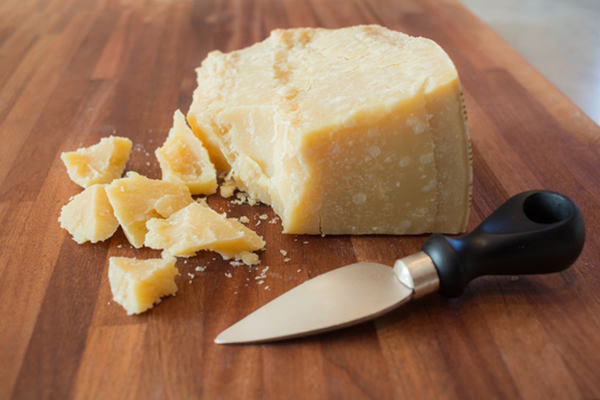 Crumbling block of Parmesan cheese with a knife next to it