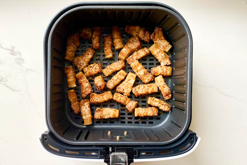 Pork belly bites in air fryer basket, midway through the air frying process